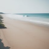【サーフィン】ボードを持って訪れる海岸 | 波が寄せる砂浜と波待ちの時間 をイメージした 広角の風景 の写真